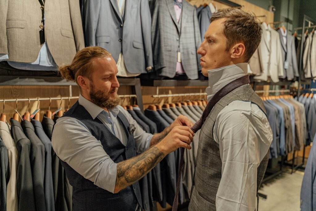 Professional tailor adjusts customer's necktie in a stylish men's suit store.